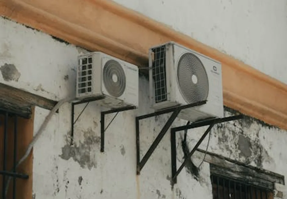 Two outdoor central AC condenser units mounted on a residential home exterior